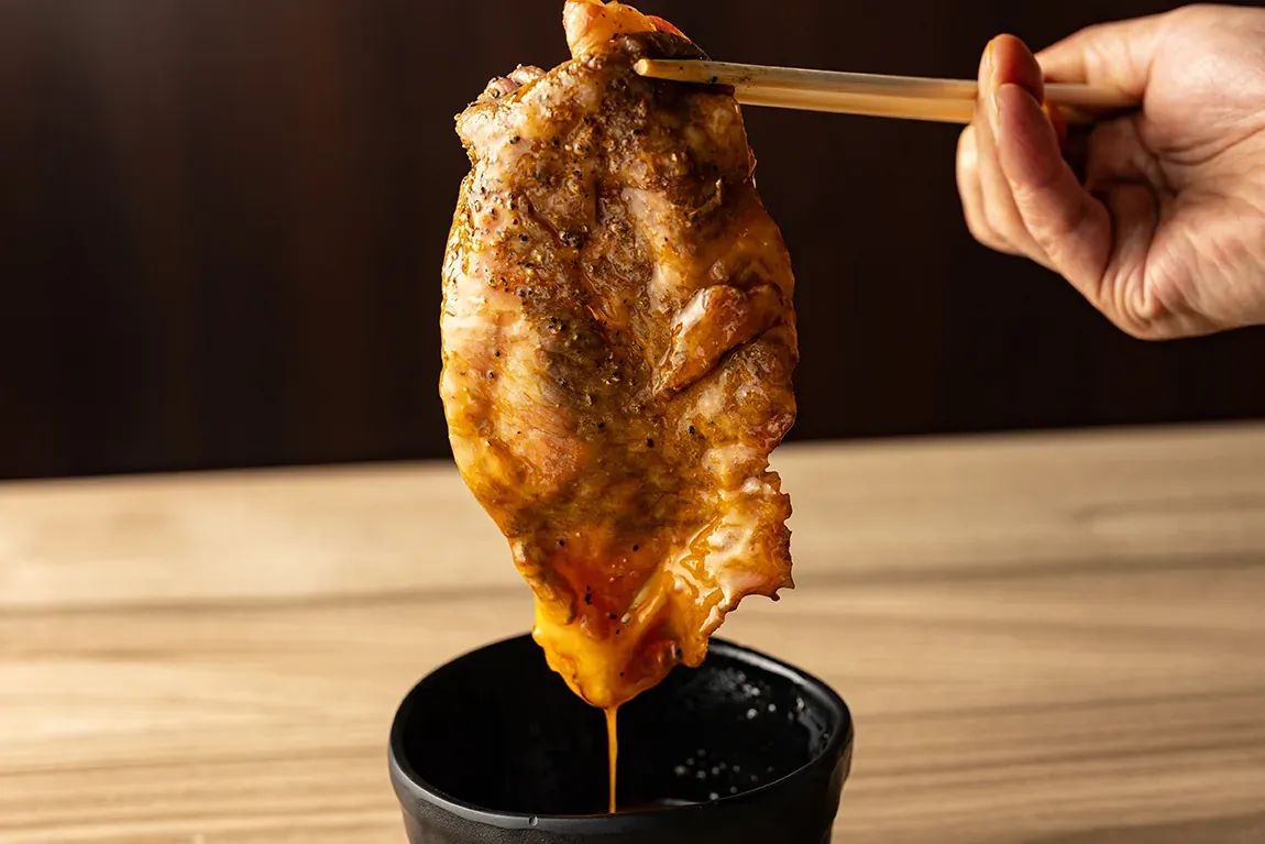 焼いた肉を箸で持ち上げ、タレにくぐらせているところ