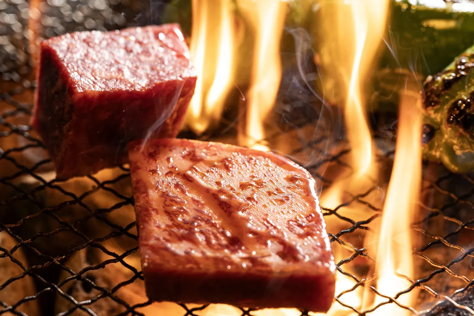 炭火の網の上で、炎を受けて焼ける角切りの牛肉