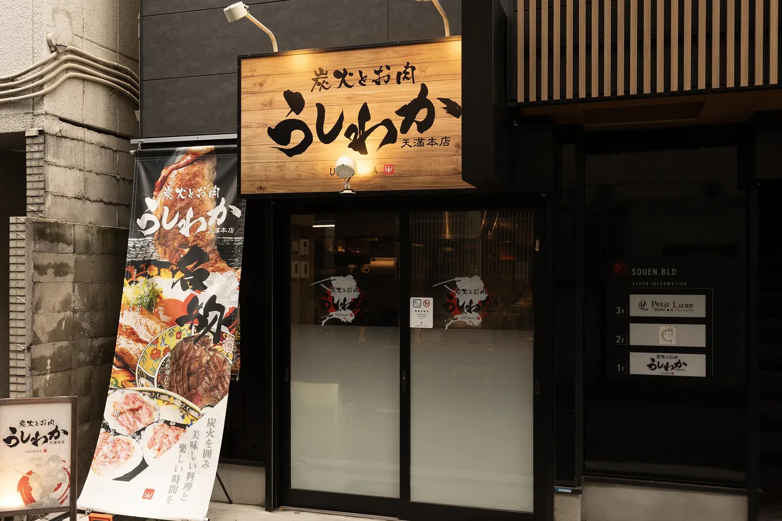 「炭火とお肉 うしわか」の看板とのぼりが立つ、天満本店の入口